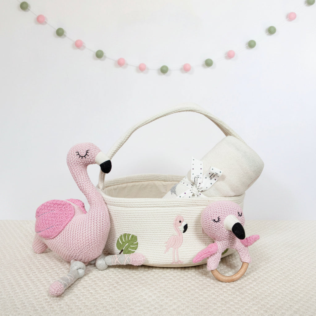 Flamingo-themed baby items including a plush toy, rattles, and a decorative banner on a light background.
