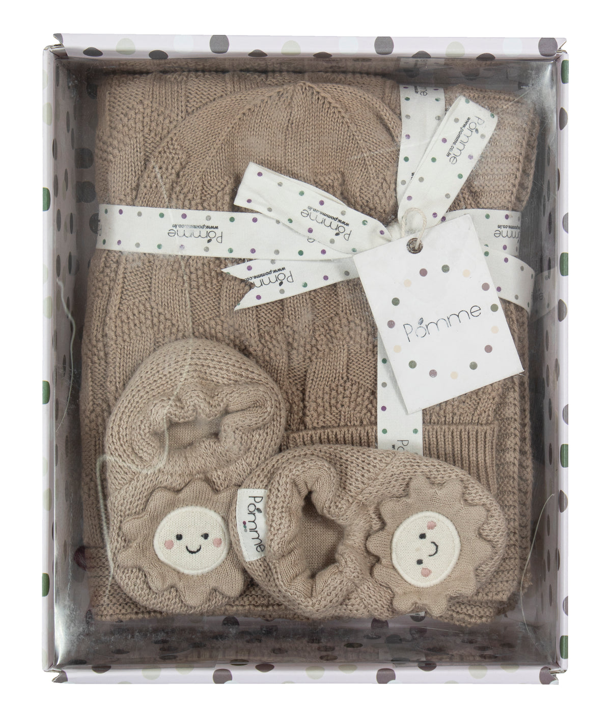 A gift box containing a pair of baby booties in a soft taupe-brown color, decorated with embroidered smiley faces and small flower appliqués. The booties are presented in a clear-lidded gift box with a white and brown polka dot patterned box, tied with a white ribbon printed with musical notes and a small card that reads 'Pomme'.